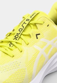 Yellow running shoe with a textured upper, featuring a white logo, lace-up design, and a cushioned white sole. Notable lightweight construction.