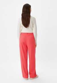 Coral wide-leg trousers with a smooth texture and two back pockets, paired with a light-colored sweater, viewed from the back.