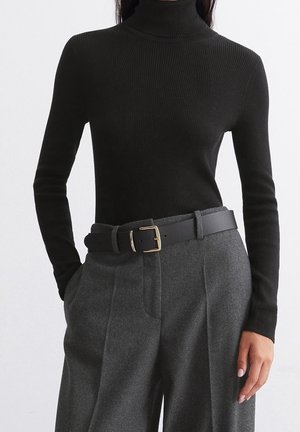 Zwarte geribbelde coltrui met lange mouwen, gecombineerd met hooggetailleerde, grijze wollen broek vastgemaakt met een zwarte riem met een gouden gesp.
