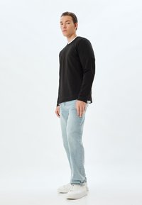 Camisa de manga larga negra combinada con jeans de rayón azul claro y zapatillas blancas. La camisa tiene un cuello redondo y una textura suave.