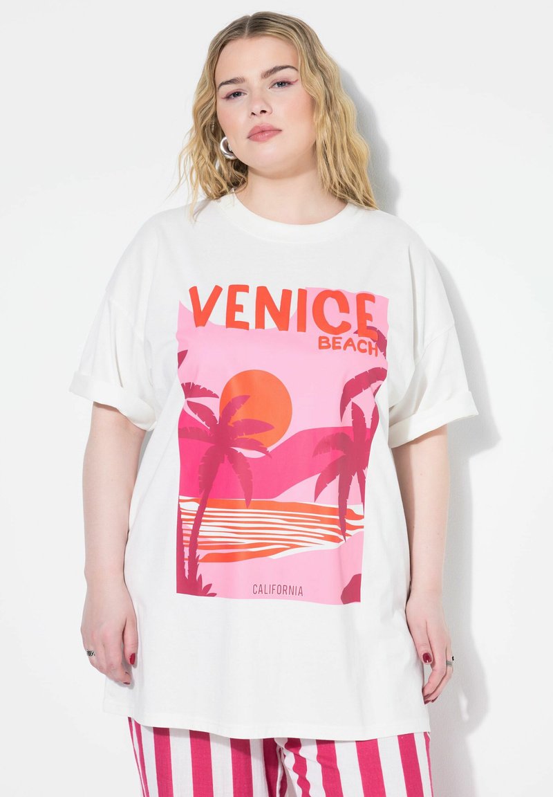 Bílý oversized tričko s růžovou a oranžovou grafikou západu slunce nad vodou s palmami. Text zní "VENICE BEACH."