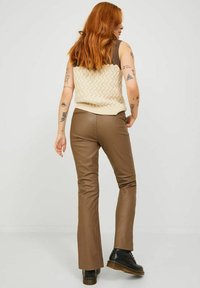 Pantalones de imitación de cuero marrón con una textura suave. La modelo lleva un suéter de punto crema, combinado con botas negras de suela gruesa.