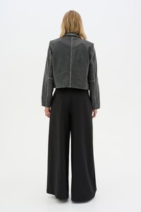 Gray cropped leather jacket with visible stitching details, paired with wide black trousers. The texture appears smooth and matte.