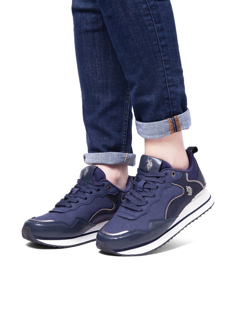 Granatowe sneakersy z mieszanym materiałem, w tym zamszem i siateczką. Wyraźne białe i srebrne akcenty na podeszwie oraz logo. Biała środkowa podeszwa.