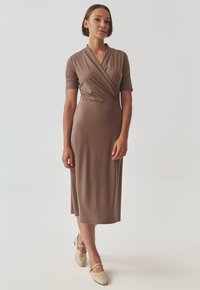 Vestido marrón hasta la rodilla en material suave y elástico, con mangas cortas y un diseño cruzado. Combinado con bailarinas de color beige claro.