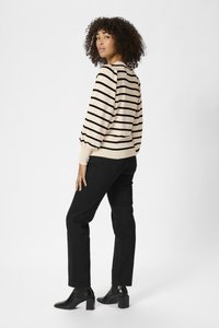 Maglione a righe beige e nere con maniche a sbuffo, abbinato a jeans neri slim e stivali neri con tacco alla caviglia. Texture liscia.
