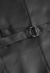 Un tejido negro con una textura suave presenta una correa central y un detalle de hebilla, diseñado para asegurar. La hebilla es metálica y rectangular.