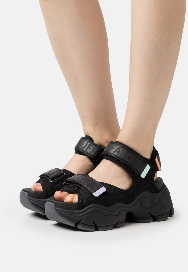 Sandali neri con cinturini regolabili, dettagli del logo audaci e suola in gomma chunky; presentano accenti colorati in menta e lavanda.
