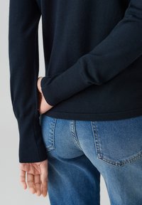 Donkerblauwe gebreide trui met lange mouwen, textuurstof en een slim fit, gecombineerd met lichtblauwe spijkerbroek met achterzakken.