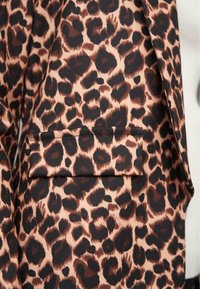 Látka s leopardím potiskem, obsahující černé a tmavě hnědé skvrny na světle hnědém pozadí, s kapsou na klopě na oděvu.