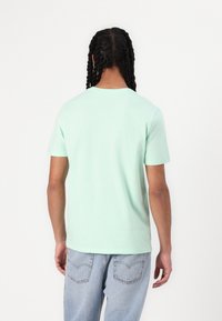 Camiseta de algodón verde menta con mangas cortas y cuello redondo, combinada con jeans de mezclilla azul claro. Diseño simple y de color sólido.