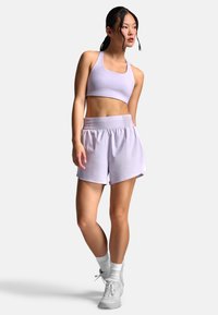 Lyse lilla sport-bh og matchende løstsiddende shorts med elastisk taljebånd. Modellen har hvide sneakers og ankellange sokker på.