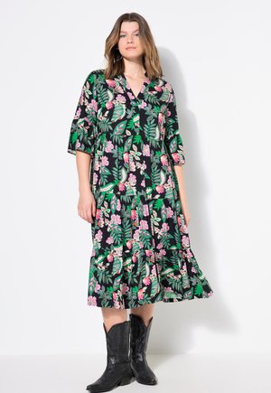 Schwarzes Blumenkleid mit kurzen Ärmeln und Rüschensaum, verziert mit grünen Blättern und rosa Blumen. Das Model trägt schwarze Cowboy-Stiefel.