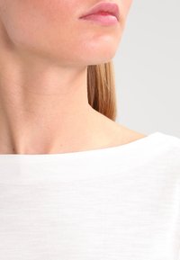 Weißer, leichter Stoff mit einer weichen Textur, der einen weit geschnittenen Hals hat. Nahaufnahme des Nacken- und Schulterbereichs mit glatter Haut.