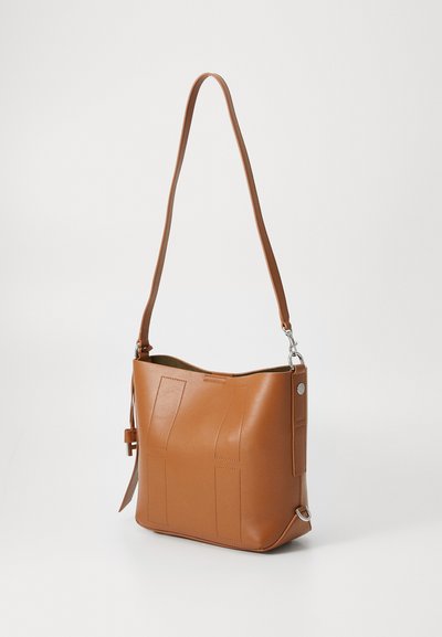 Sac à épaule en cuir tan avec une texture lisse, présentant un design décontracté, des patches rectangulaires et un accent en métal argenté.