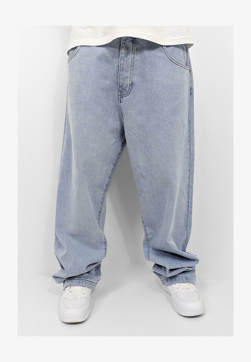 Gai zila džinsa baggy bikses ar brīvu piegriezumu, ar priekšējiem kabatām un sapostītām potītēm, apvienotas ar baltām kedām.