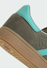 Baskets Adidas avec une tige grise texturée, des accents turquoise, et une semelle en caoutchouc beige ornée d'un motif en losange et du logo de la marque.
