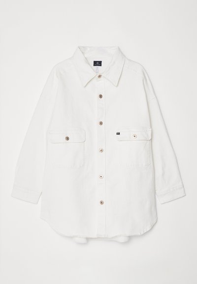 Camicia bianca con bottoni in cotone, colletto, due taschini frontali e quattro bottoni sulla parte anteriore; vestibilità ampia e maniche con risvolto.