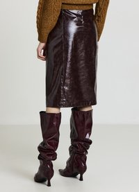 Jupe crayon en cuir bordeaux à la finition lisse, associée à des bottes bordeaux molles montant jusqu'aux genoux et à un pull en maille marron texturé.