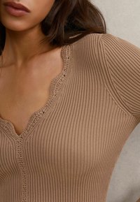 Top a maniche lunghe a coste color marrone chiaro con scollo a V smerlato e tessuto testurizzato. Primo piano che mostra le cuciture dettagliate al collo.