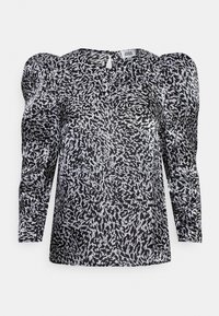 Blusa com padrão preto e branco, mangas bufantes, decote redondo e chave na parte de trás. Feita de um tecido leve e texturizado.