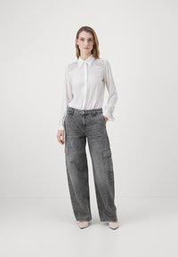 Camicia bianca a maniche lunghe con dettagli plissettati sulle spalle, abbinata a jeans cargo grigi a taglio largo con tasche laterali e gamba dritta.