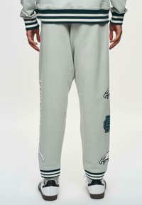 Lysegrå sweatpants med stribede manchetter, med logoer på siden. Materialet er blødt med en glat tekstur, og designet har en afslappet pasform.