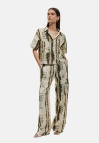 Tweedelig outfit bestaande uit een kortemouwen overhemd met knopen en een broek met wijde pijpen. Gemaakt van een geweven stof met een groen en bruin streepjespatroon.