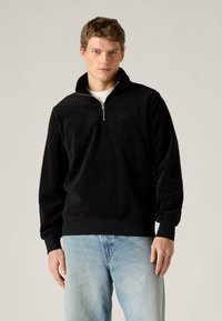 Μαύρο φλις πουλόβερ με γιακά τετάρτου φερμουάρ, ριμπ μανσέτες και στρίφωμα. Διαθέτει διακριτικό λογότυπο στο στήθος και άνετη εφαρμογή. Φορεμένο κάτω από τζιν τζιν.