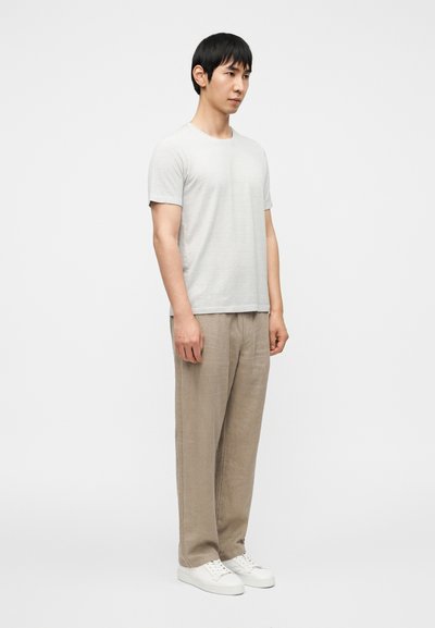 Ανοιχτό γκρι κοντομάνικο μπλουζάκι, μπεζ παντελόνι από λινό και λευκά αθλητικά παπούτσια. Η εμφάνιση έχει χαλαρή εφαρμογή με απλή υφή και διακριτικό σχεδιασμό.