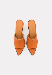 Πορτοκαλί δερμάτινα ανοιχτά κομμάτια με μυτερή μύτη και ευρεία μπροστινή λωρίδα. Διαθέτουν λεία υφή και μαύρη σόλα. Εσωτερική σόλα με σήμα.