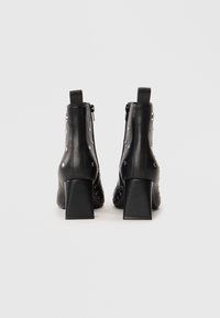 Black leather ankle boots with a square heel, featuring metallic studs, black zippers, and a sleek design. Textured finish at the back.