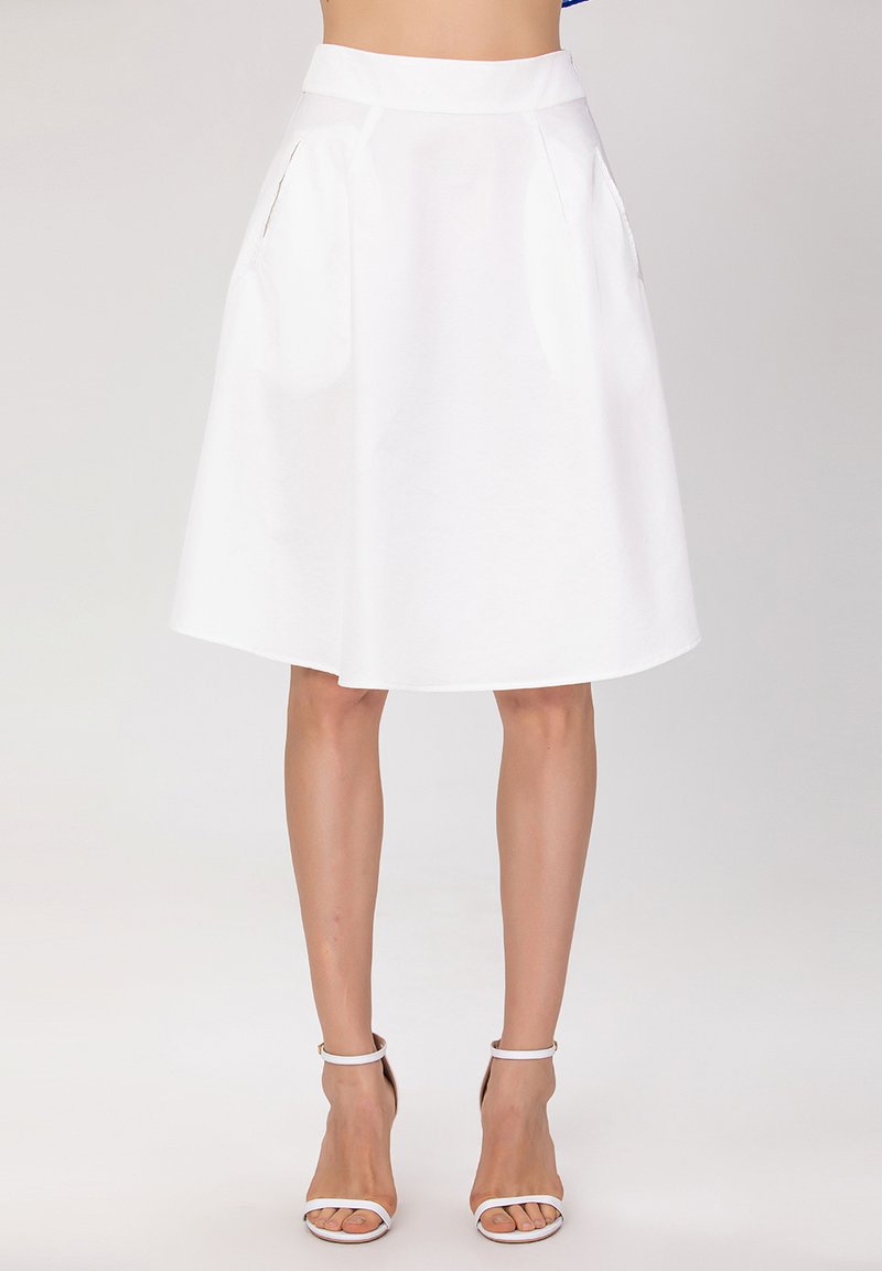 Jupe A-line blanche, longueur genou, avec poches avant, en tissu lisse. Associée à des sandales blanches à bride de cheville.