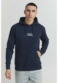 Navy hoodie made of cotton with a front pocket, adjustable drawstrings, and white striped logo detail on the chest. Soft texture.