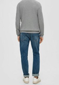 Grauer Strickpullover mit gerippten Bündchen, kombiniert mit blauen Denim-Jeans in lässiger Passform und umgeschlagenen Bündchen. Weiße Turnschuhe werden getragen.