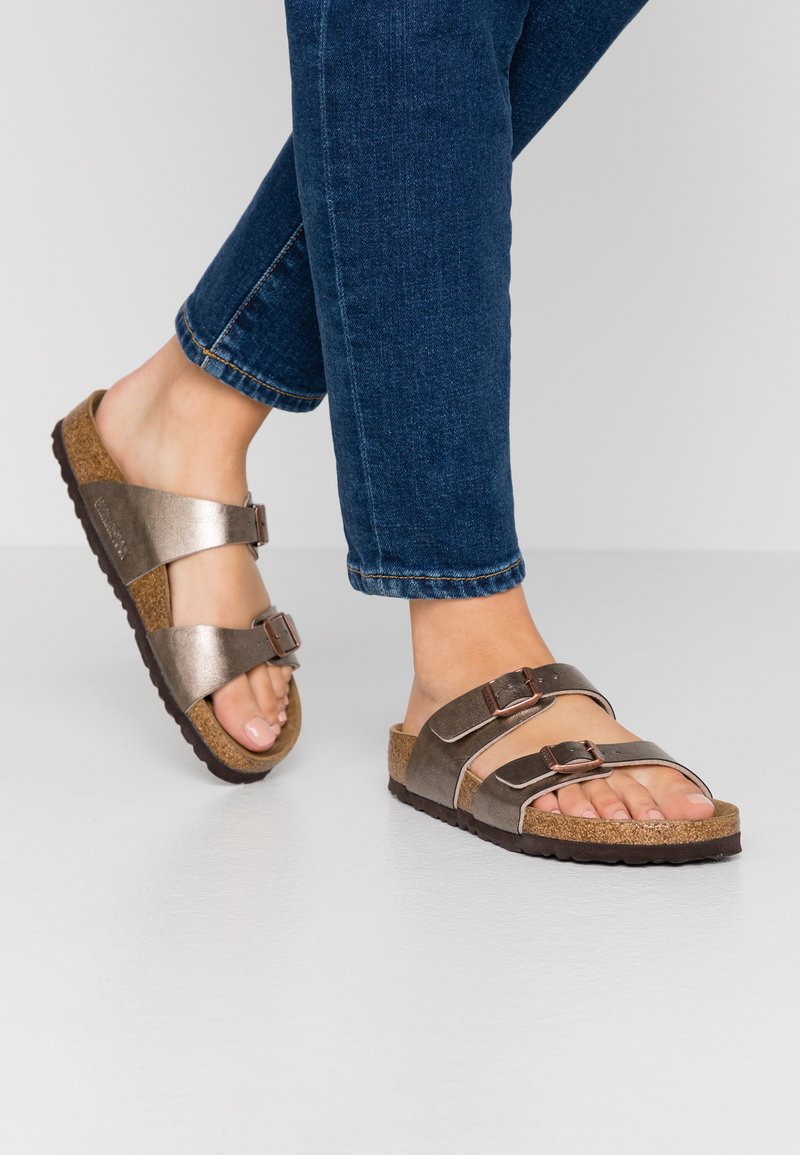 Braune und metallic-silberne Riemchensandalen mit zwei verstellbaren Riemen, Korkfußbett, strukturiertem Gummisohle und rundem Zehendesign.