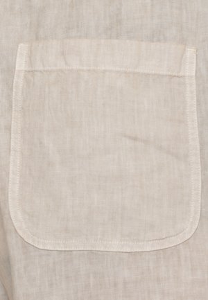 Tessuto di lino beige con tasca quadrata cucita, con cuciture visibili lungo i bordi e una base leggermente arrotondata.
