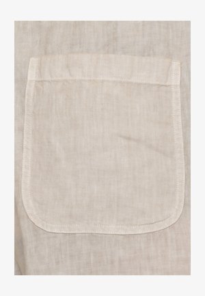 Tessuto di lino beige con tasca quadrata cucita, con cuciture visibili lungo i bordi e una base leggermente arrotondata.