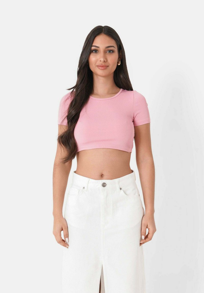 Top corto a coste rosa chiaro con maniche corte, abbinato a una gonna di jeans bianca a vita alta con spacco frontale e bottone in metallo.