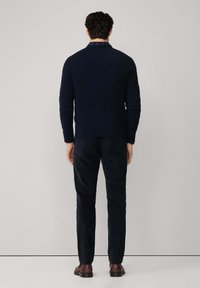 Maglione a coste blu navy con collo alto, abbinato a pantaloni blu navy scuri. Tessuto liscio con una vestibilità aderente e minimi accenti in metallo.