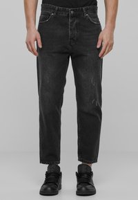 Zwarte denim jeans met een relaxed fit, met lichte schade, vijf zakken en contrasterende stiksels. Gecombineerd met zwarte sneakers.