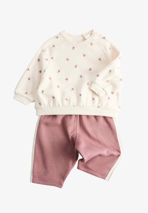 Cremefarbenes Langarmoberteil mit kleinen rosa Blumen kombiniert mit mauvefarbenen Shorts mit weißen Seitenstreifen, flach auf weißem Hintergrund gelegt.