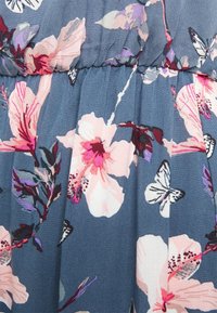 Blommönstrad tyg i nyanser av blått visar rosa och lila blommor, med fjärilsaccenter. Materialet har en mjuk, texturerad yta.