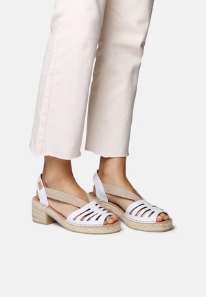 Sandalia blanca con diseño recortado, suela de yute trenzado estilo espadrille, tira de color beige texturizada, tacón bajo y punta abierta.