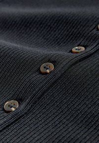 Közeli felvétel fekete bordázott szöveten, négy látható kerek teknősbéka gombbal, amelyek függőlegesen varrva vannak.