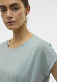 Jasnoniebieska, prążkowana koszulka z krótkimi rękawami i okrągłym dekoltem. Gładka tekstura z delikatnym połyskiem. Zbliżenie na tors.