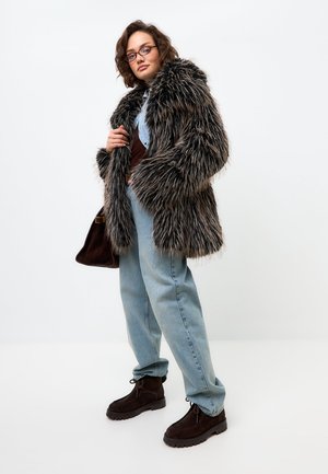 Kožich z umělé kožešiny v tmavě šedé a hnědé barvě s dlouhou, huňatou texturou; doplněný světle modrými oversized džínami a tmavě hnědými kotníkovými botami.