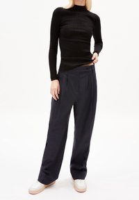 Haut long à rayures noir associé à un pantalon large bleu marine. Les chaussures sont crème avec une semelle beige. Textures lisses et coupe ajustée.