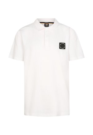 Jongen staat, draagt een wit poloshirt, spijkershorts, witte sokken en witte sneakers tegen een effen lichte achtergrond.
