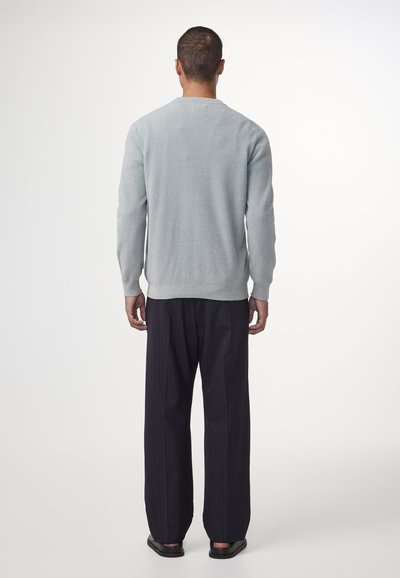 Hellblau strukturierter Pullover mit langen Ärmeln, gerippten Bündchen und Rundhalsausschnitt, kombiniert mit dunkel gestreiften Hosen und schwarzem Schuhwerk.